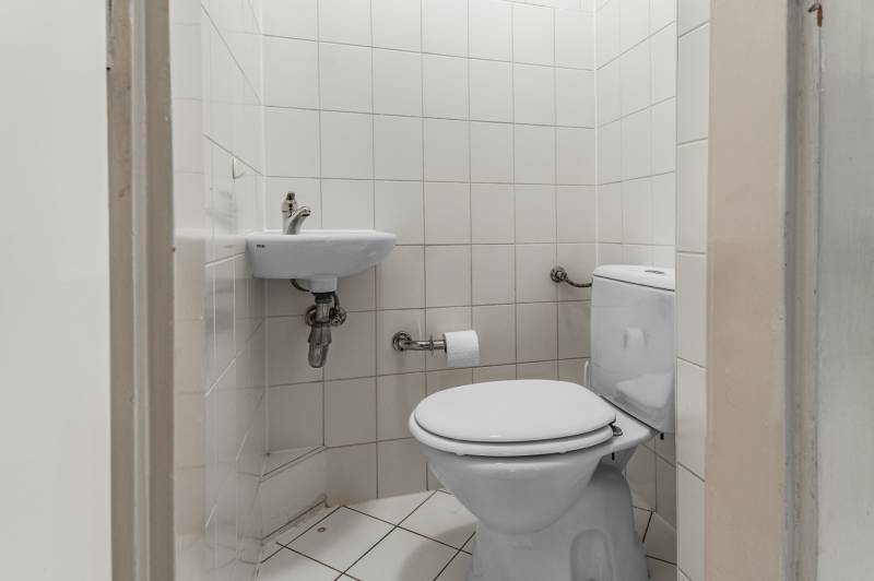 A toilet with white tiles in a 3-room apartment, a small sink area, and a toilet.