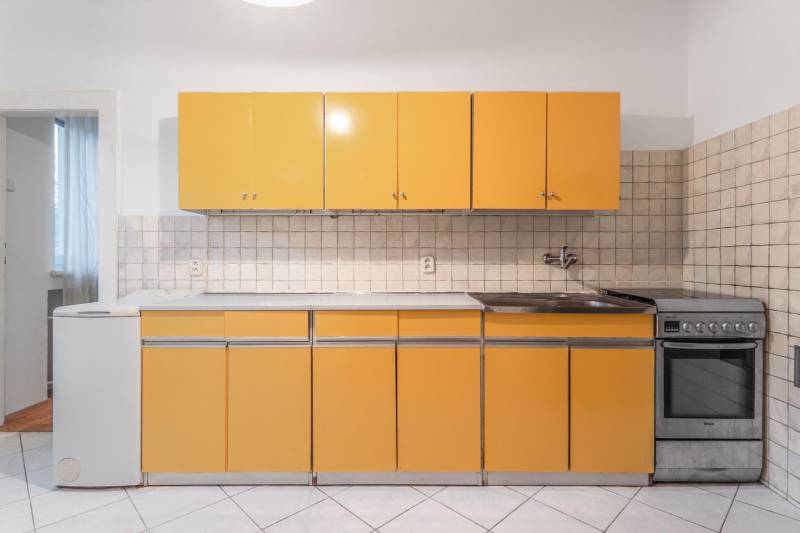 A kitchen in a 3-room apartment with orange cabinets and white tiles.