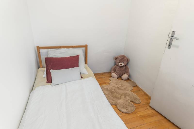 A bed with pillows, a plush teddy bear, and a bear-shaped rug on a floor with wooden decor.