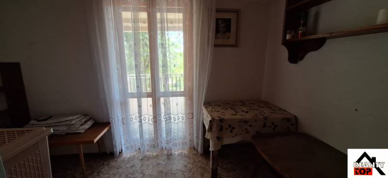 A room in a family house with a window, a curtain, and a table with a tablecloth.