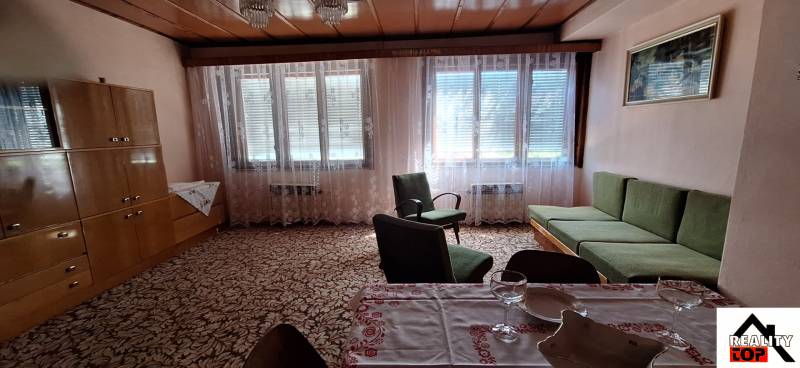 Living room in a family house with a sofa, armchairs, a wardrobe, and covered windows.