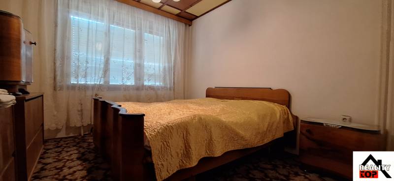 A bedroom with a bed, wardrobe, carpet, and a window with a lace curtain in a family house.