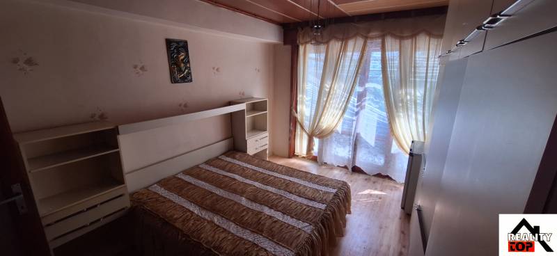 Bedroom in a family house with a bed, integrated shelf, and curtains over the windows.