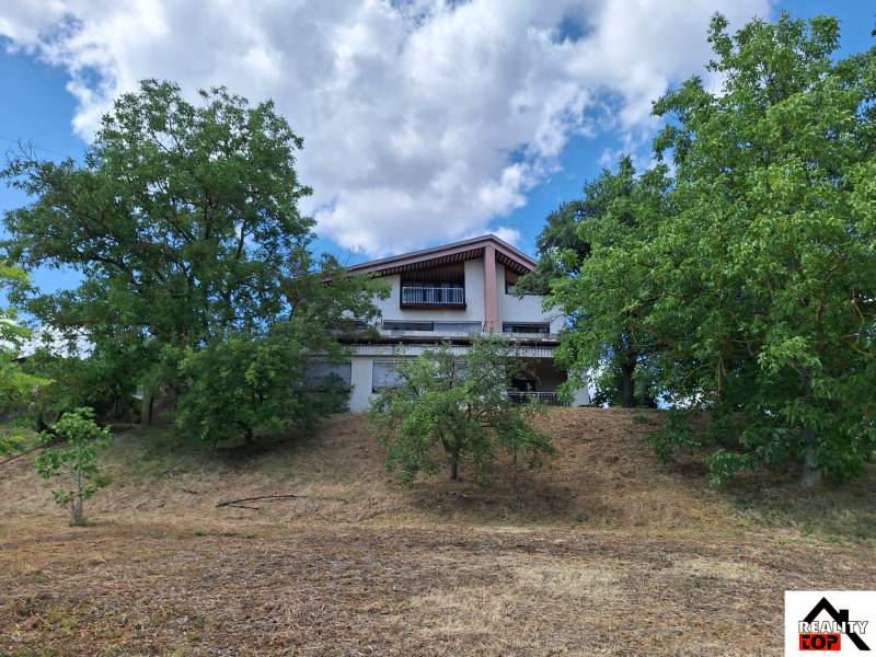 A family house in Nová Bašta surrounded by greenery, on a gentle slope under the sky.