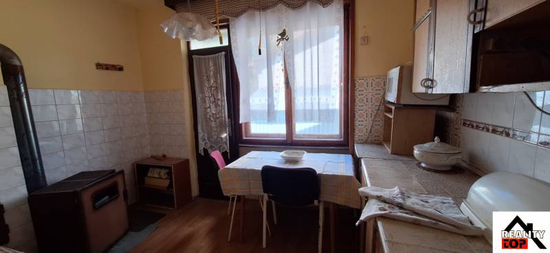 A kitchen in a family house with a wooden decor floor, a stove, and a table by the window.