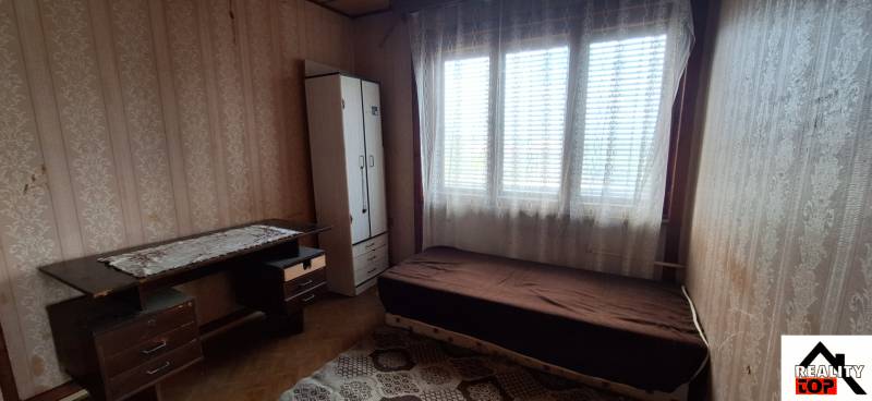 A room in a family house with a bed, table, and wardrobe, featuring a wooden floor decor.