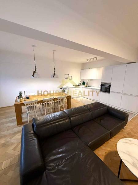 Living room with kitchen in a 4-room apartment, wooden decor flooring, spacious sofa and dining table.