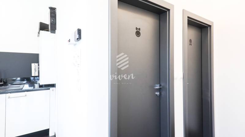 Interior of commercial premises with two doors marked with symbols and a kitchen unit.