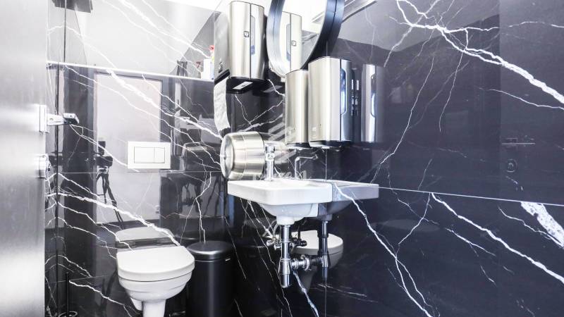 A bathroom with black marble tiles, a sink, a toilet, and soap dispensers in commercial premises.