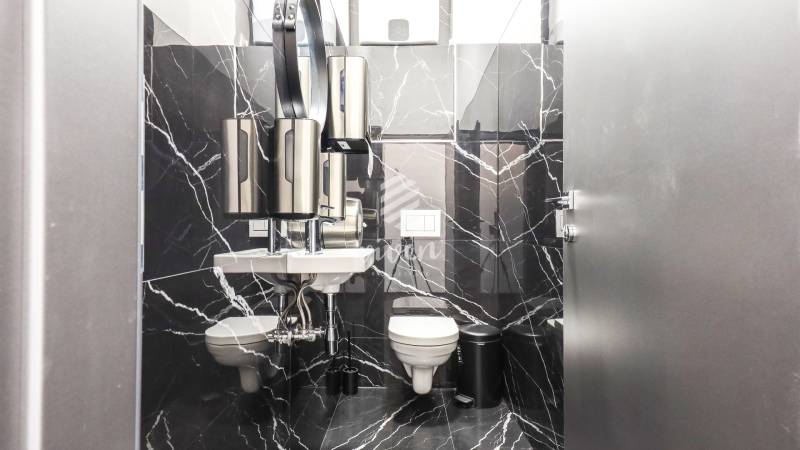 A restroom with black marble tiles, stainless steel accessories, and a sink in commercial premises.