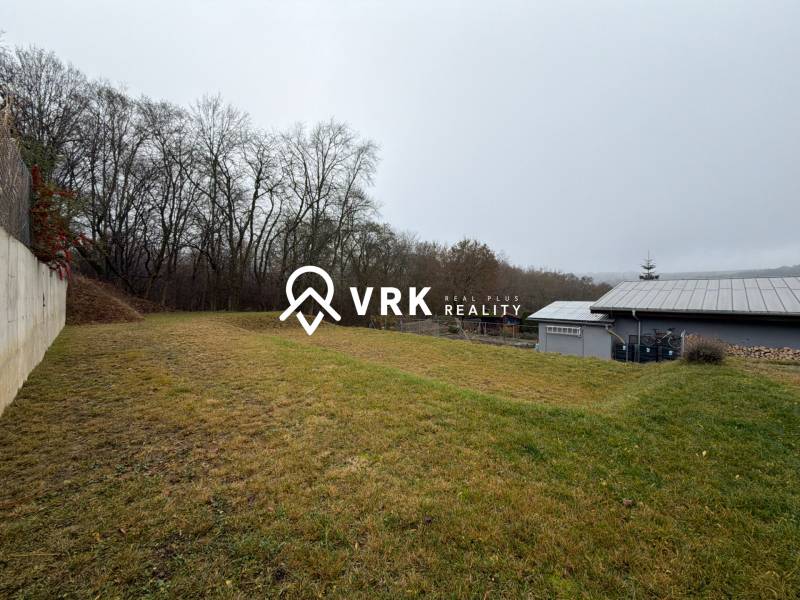 The garden of a family house in Ploské with a grassy area, a fence, and an adjacent forest.