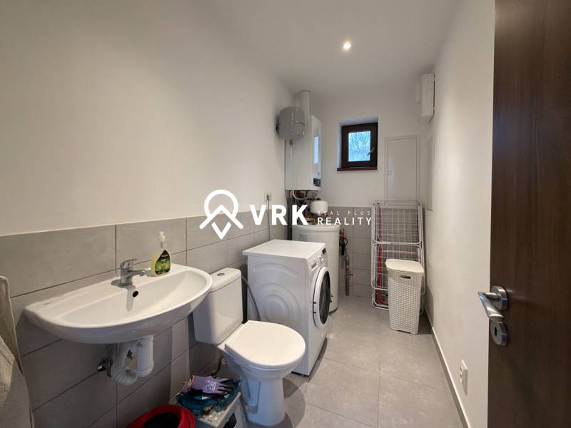 Bathroom in a family house with a washing machine, sink, and toilet, tiled floor.