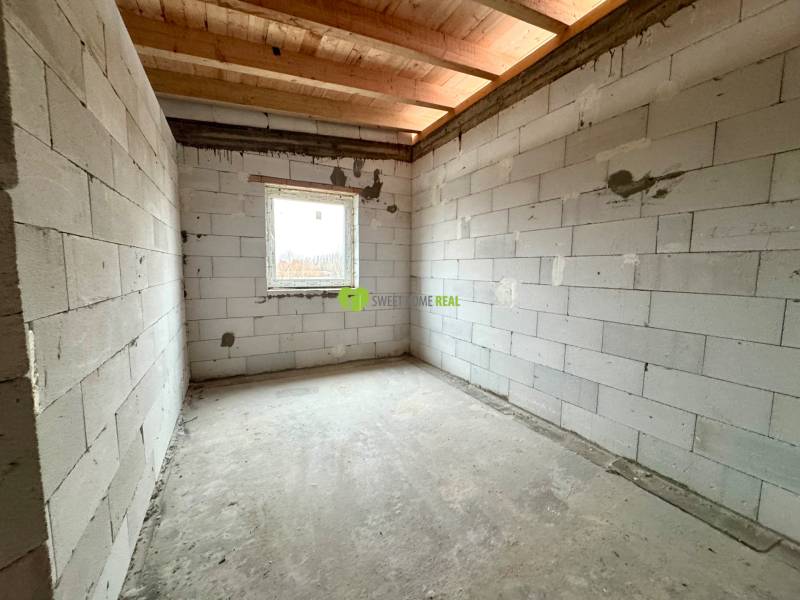 An unfinished room in a family house with a concrete floor and a window offers space for completion.