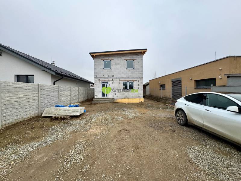 The construction process of a family house on Hviezdna Street in Čaňa. Surrounding buildings and a car.