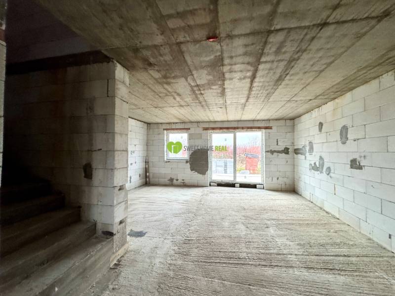 Unfinished interior of a family house with a view of the terrace through a large window.