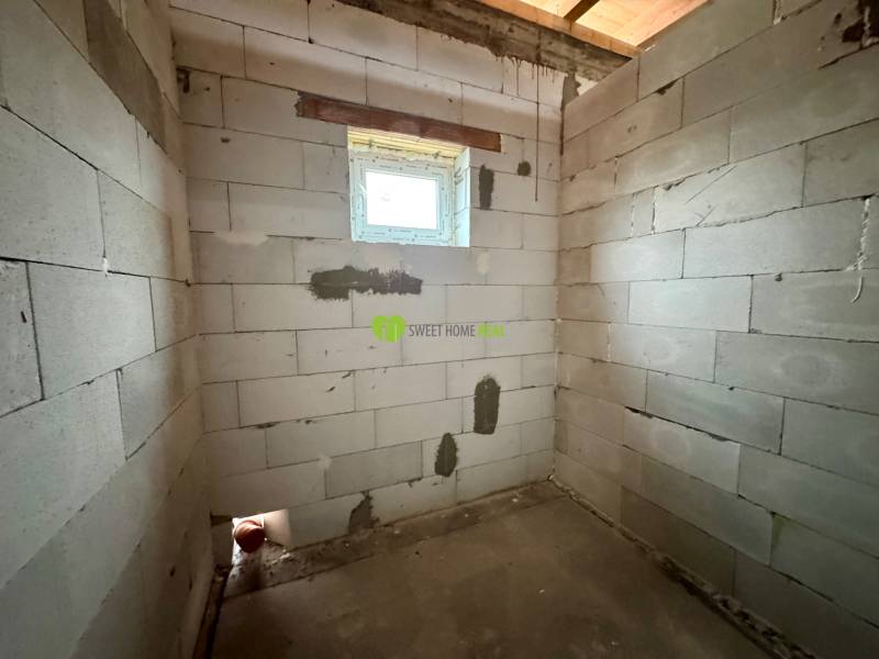 A room with a brick wall in a family house, with a small window and a concrete floor.