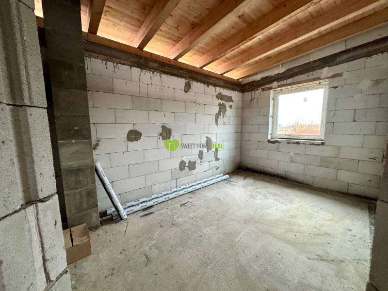 An unfinished room in a family house with a concrete floor, wooden ceiling, and a window.