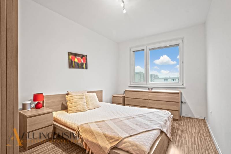 A bright bedroom with wooden decor, a flower painting, and a view of the city.