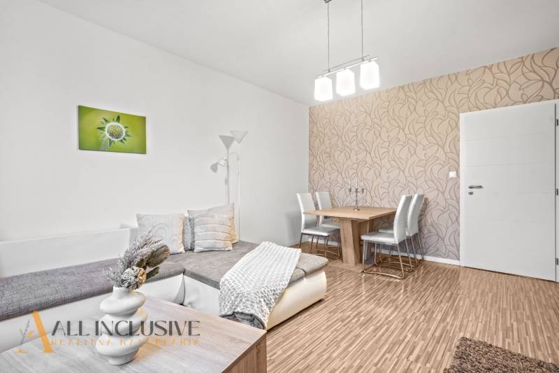 Living room with wood-patterned flooring, a sofa, and a dining table in a three-room apartment.