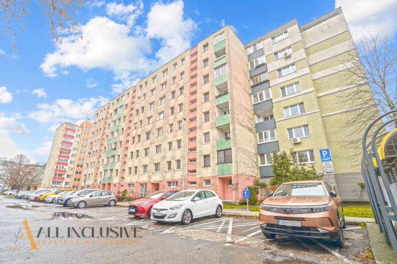 Apartment building in Bratislava - Vrakuňa, parking lot with cars and blue sky above a 3-room apartment.