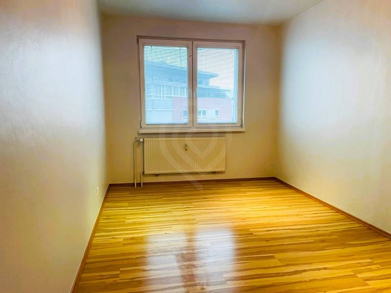 A room with a wooden decor floor in a 3-room apartment, large window, and radiator.
