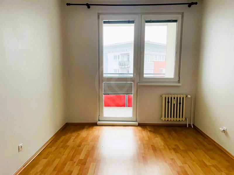 A room in a 3-room apartment with a wooden decor floor and balcony doors.