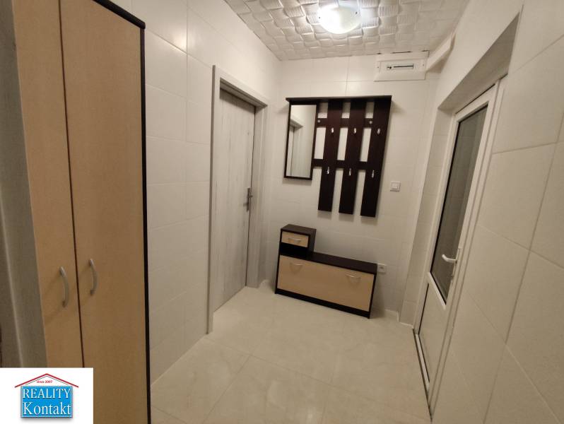 A hallway in a 2-room apartment with white walls, a built-in wardrobe, and a coat rack.