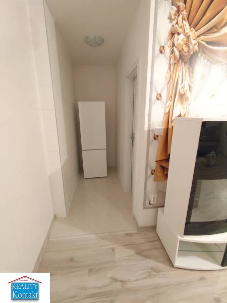 A hallway in a 2-room apartment with a wooden decor floor and a refrigerator.