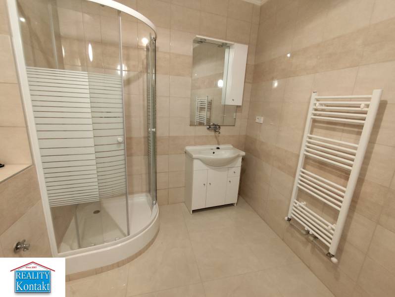 A bathroom in a 2-room apartment with a corner shower and white furniture.