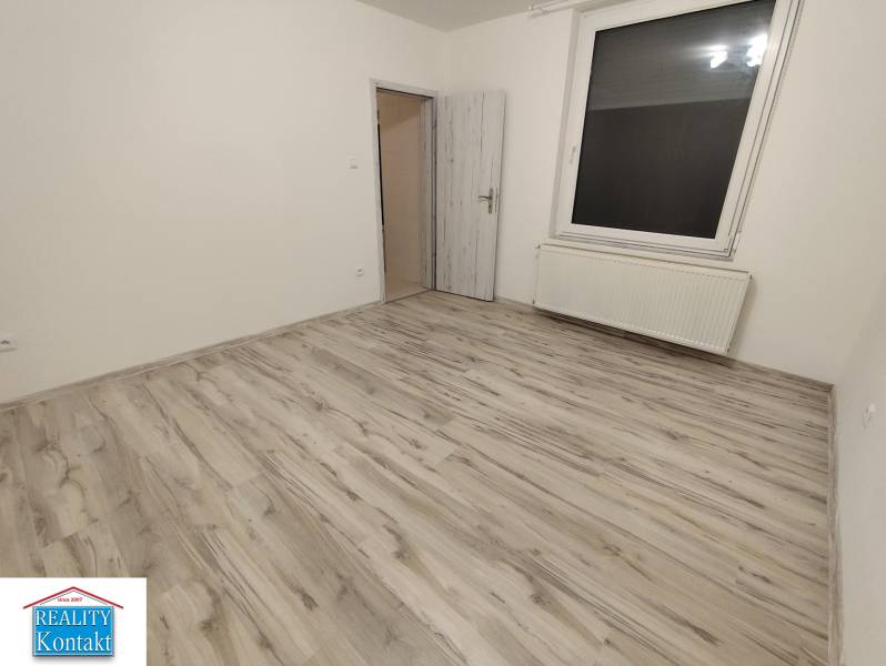 A room in a 2-room apartment with a wood-patterned floor and a large window.