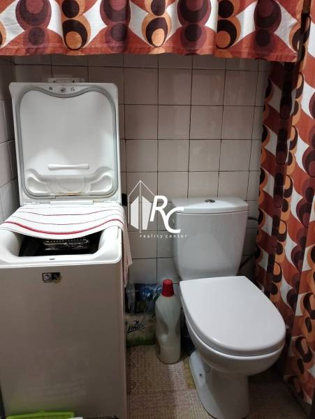 Bathroom in a 3-room apartment with a washing machine, toilet, and colorful curtain.