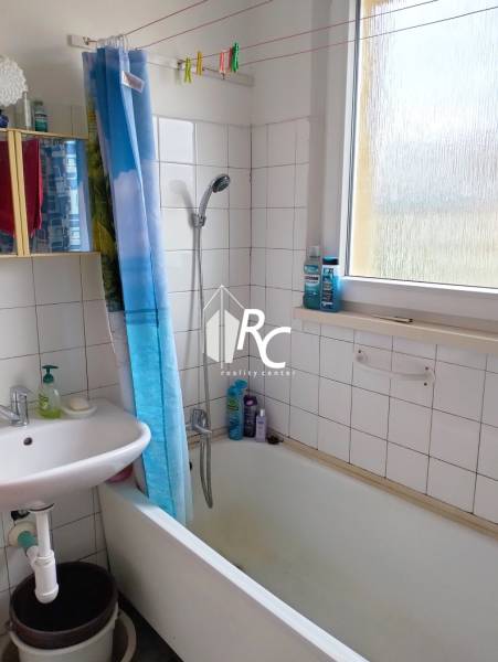 A bathroom in a 3-room apartment with a shower bath, curtain, and sink.