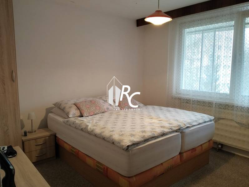 A bedroom in a 3-room apartment with a bed, a window, and wooden furniture.