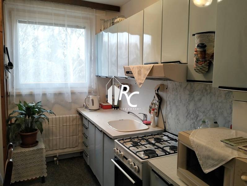 A kitchen with white cabinets, a window, a stove, and a houseplant in a 3-room apartment.