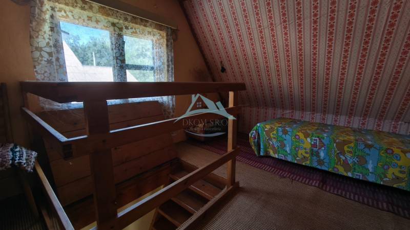 Interior of a cabin with wooden railing, a bed with colorful covers, and floral curtains.