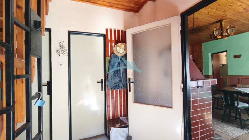 Interior of a cabin with a door, a clothes hanger, a tiled stove, and furniture.