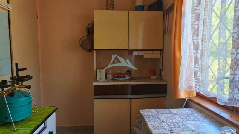A kitchen in a cottage with a gas stove, a curtain, and cabinets.