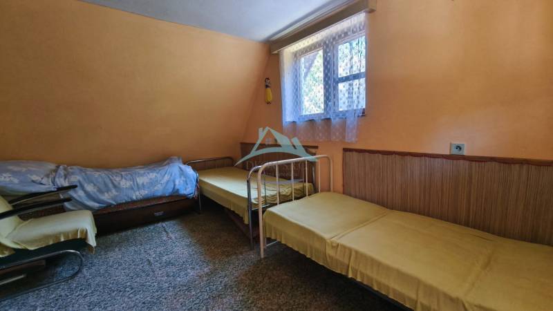 Interior of a cabin with three beds, carpet, window with a white curtain, simple furniture.