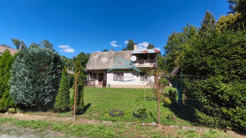 A cottage in Dolné Strháre with a garden, surrounded by greenery and a blue sky.