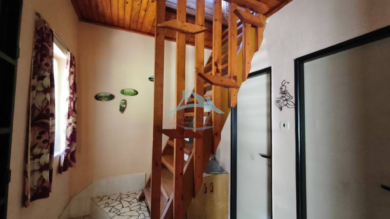 A cottage with a wooden staircase, floral curtains, and wall decorations.