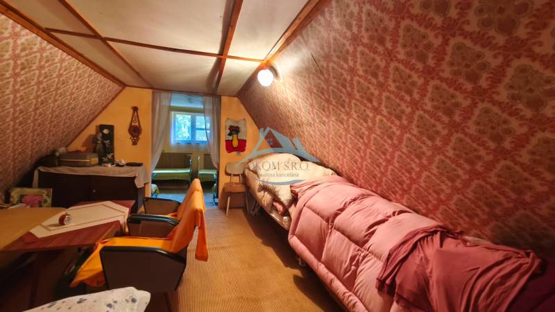 Attic room with a bed, chairs, and patterned wallpaper in a cottage.