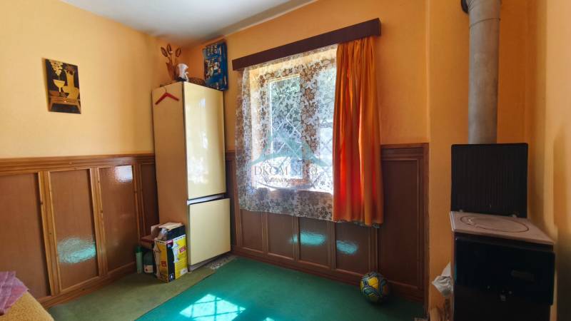 Interior of a cottage with colorful walls, a stove, and a refrigerator under a window with curtains.