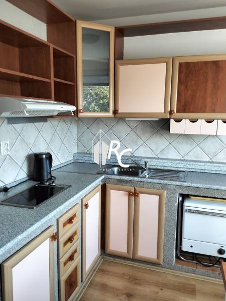A kitchen in a studio apartment with a kitchen unit and a floor with a wooden decor.