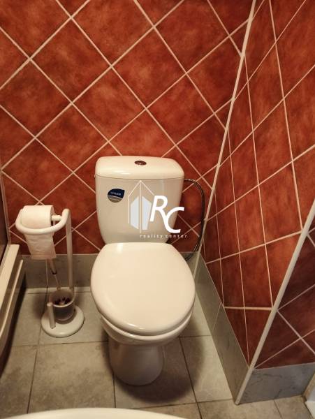 Bathroom in a studio apartment with a toilet, brown tiles, and a stone-patterned floor.