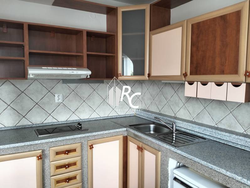 Kitchen in a studio apartment with a countertop, cabinets, and tiles on the wall.