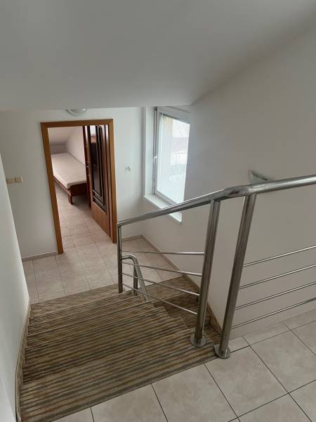 A staircase with carpet and railing leads to a room with a bed in a family house.