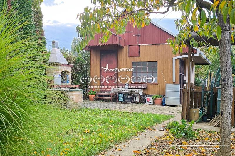 Wooden garden house with a grill surrounded by greenery and a paved walkway in Trnava.