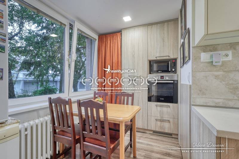 Dining area in a 3-room apartment with wood-patterned flooring, large windows, and a built-in oven.