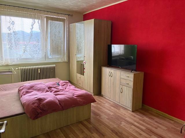 A bedroom in a 3-room apartment with a red-colored wall, a wooden decor floor, and furniture.