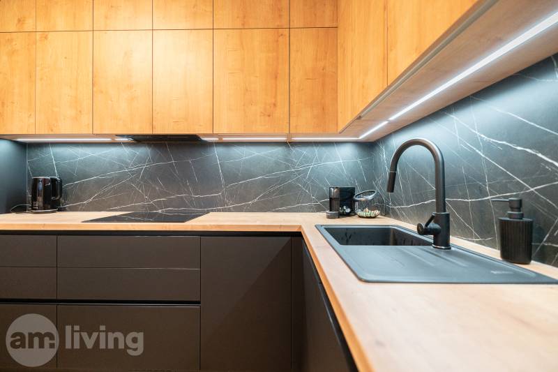 A kitchen in a 3-room apartment with contrasting dark tiles and backlighting, and a floor with a wooden decor.
